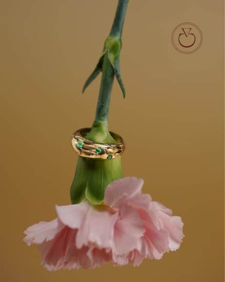 La bague bombée en or jaune Alba sertie d'émeraudes et diamants est sur une fleur